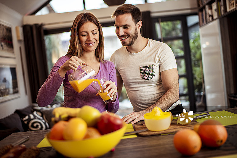 年轻妻子在家中将鲜榨橙汁倒入碗里，丈夫在她身旁图片素材