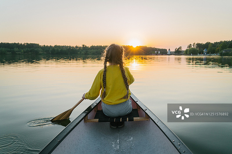 女孩在日落时于湖上划独木舟图片素材