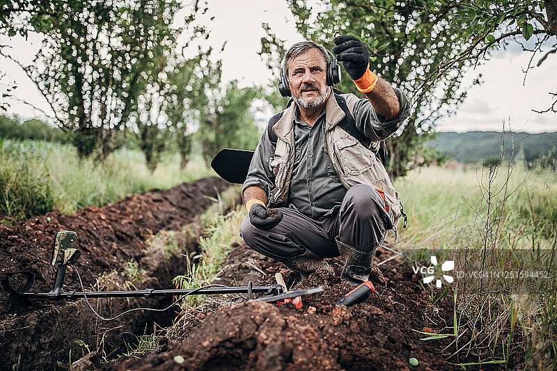 年长的男人用金属探测器在地上发现埋藏物图片素材