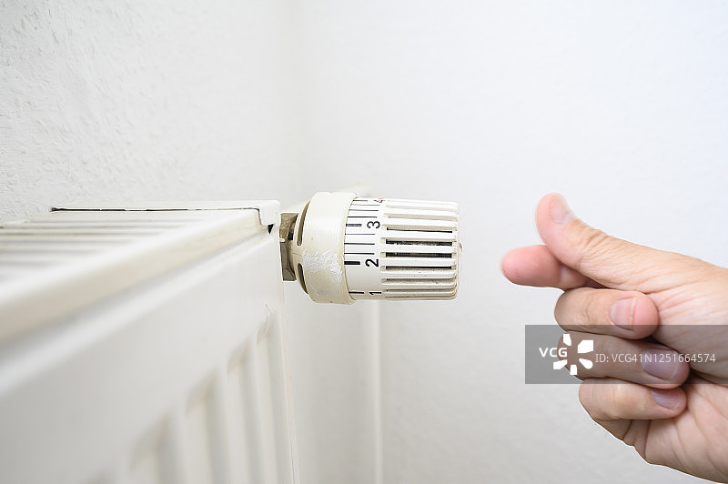 男人手在散热器旁做出省钱手势图片素材