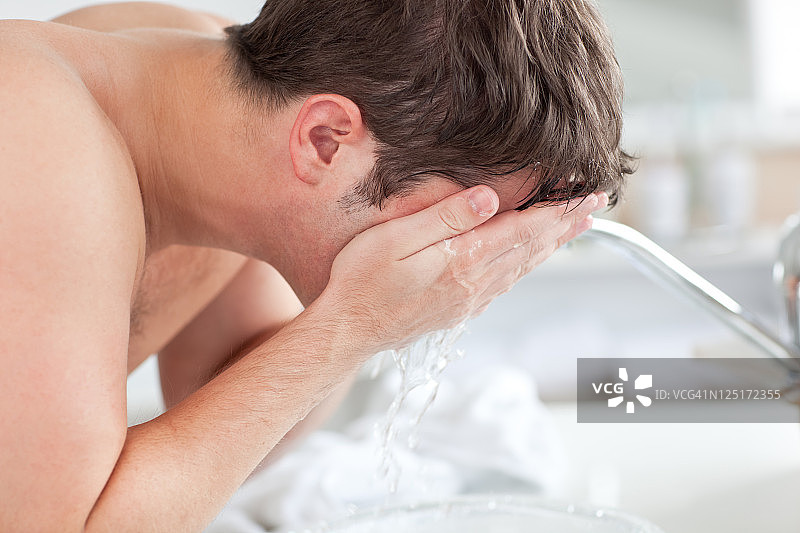 刮胡子后在浴室里往脸上喷水的可爱男人图片素材