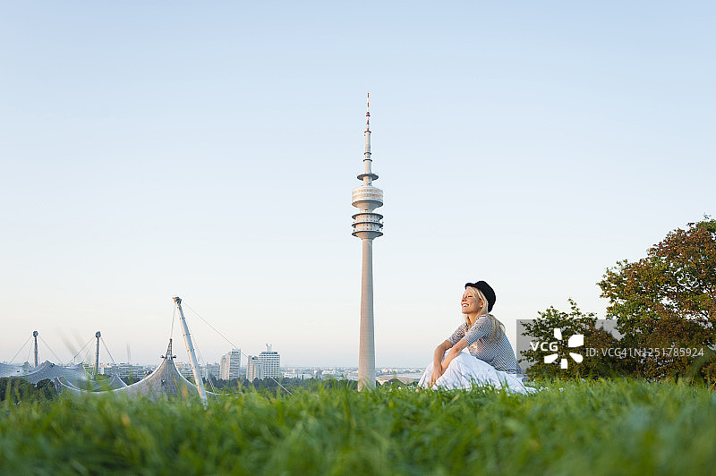 坐在慕尼黑草地上，背景是奥林匹克塔的年轻女子，德国图片素材