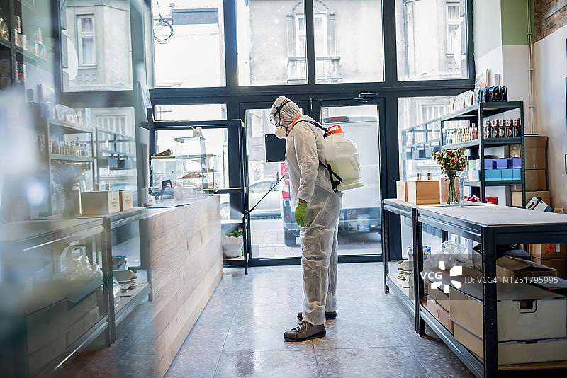 穿着防护服的男人在商店内消毒和喷洒图片素材