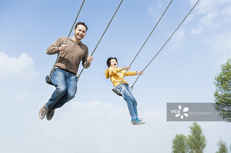 快乐的父子在蓝天下荡秋千图片素材