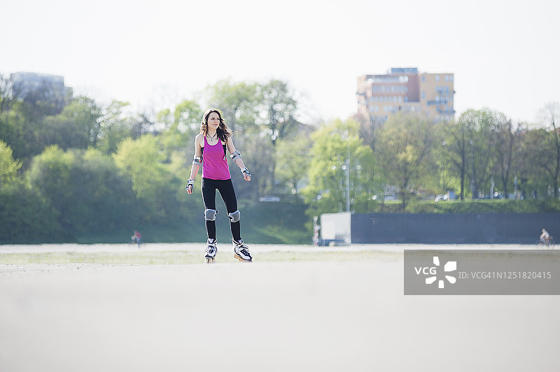 阳光明媚的日子里，年轻女人在公园陆地上玩轮滑图片素材