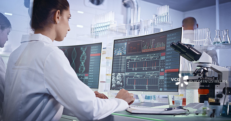 研究团队研究DNA突变，前景是带有DNA螺旋的电脑屏幕图片素材