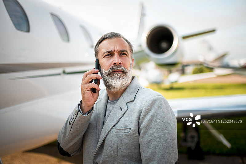 商人站在停在机场的飞机旁使用智能手机图片素材
