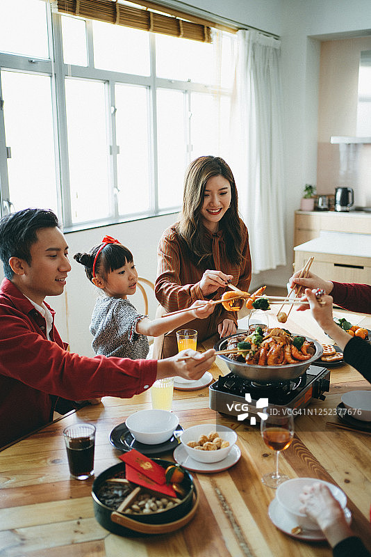 喜庆的亚洲家庭欢度中国新年，团圆饭享用美味的传统盆菜图片素材
