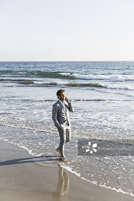 赤脚商人于加利福尼亚州洛杉矶阳光明媚的海浪中用智能手机交谈图片素材