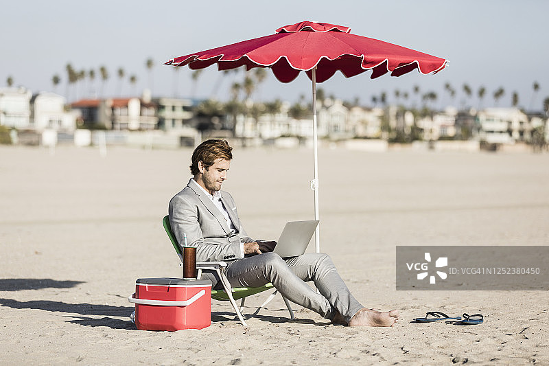 在阳光明媚的加利福尼亚州洛杉矶海滩上使用笔记本电脑的赤脚商人图片素材