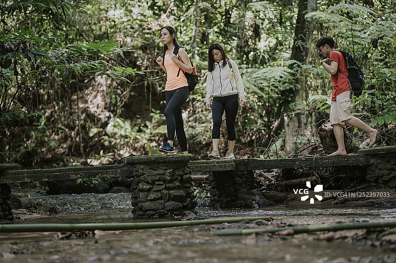 三位亚洲华裔朋友在森林中穿过河上的桥梁丛林徒步旅行图片素材