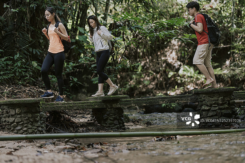 三位亚洲华裔朋友在森林中穿过河上的桥梁丛林徒步旅行图片素材