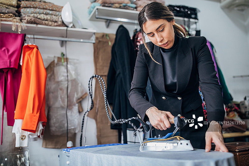 女时装设计师在她的工作室熨烫衣服图片素材