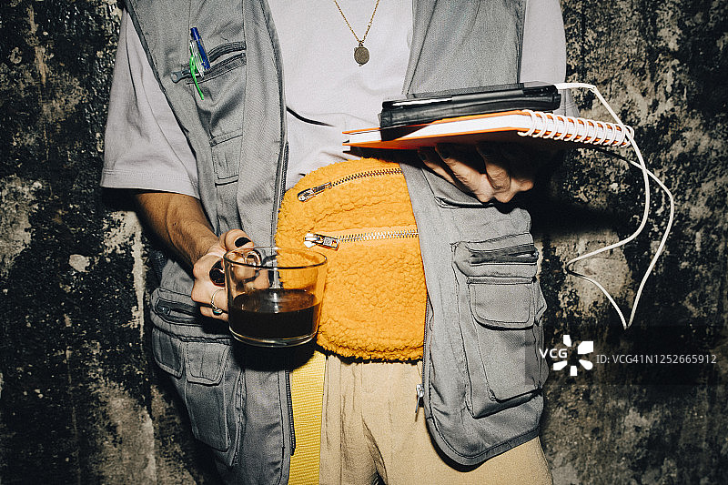 在工作场所靠墙站立，手拿咖啡的商人的腰部特写图片素材