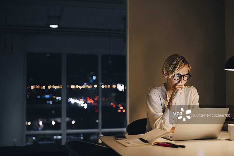 敬业的成熟女商人坐在联合办公空间的发光桌子旁，使用笔记本电脑图片素材