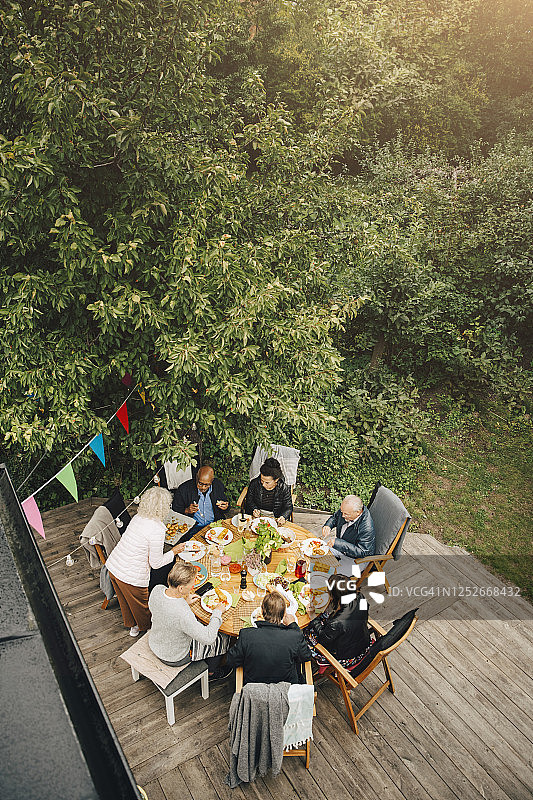 高角度的妇女服务朋友坐在餐桌在花园聚会在后院图片素材