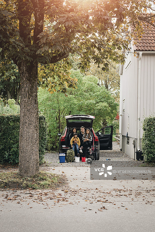 父母和女儿们坐在电动汽车的后备箱里图片素材