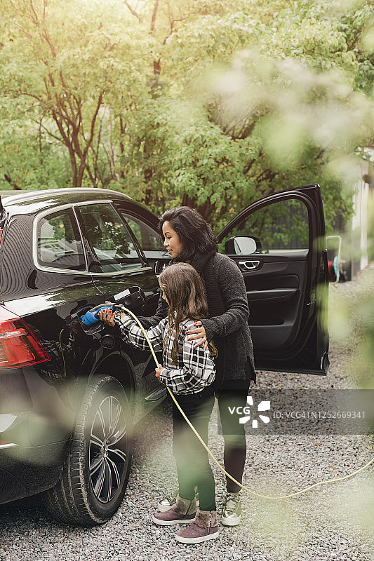 中年妇女教女儿在充电站给电动汽车充电图片素材
