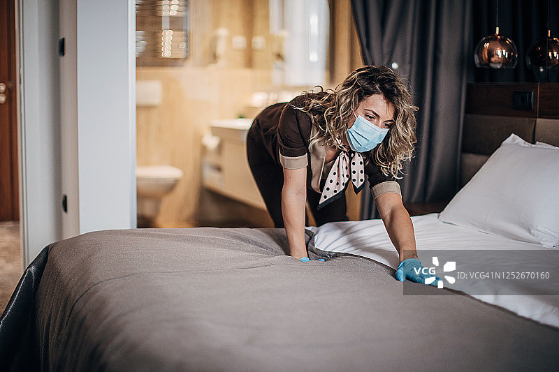 一位年轻客房服务员在酒店工作时戴着防护口罩和手套图片素材