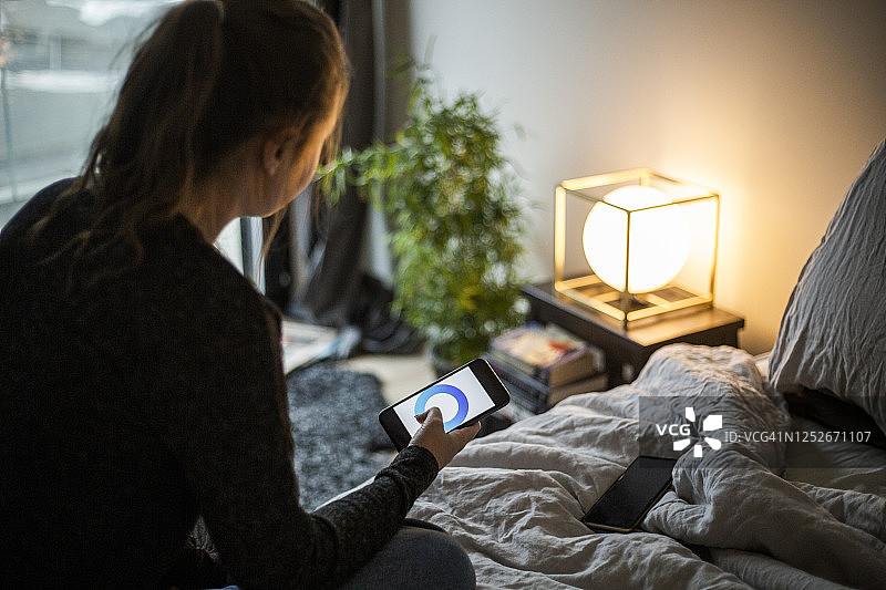 少女在智能家居的卧室里使用智能手机应用程序调整照明设备图片素材