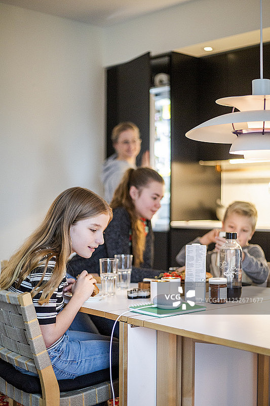 女孩在现代家居中与家人围坐在桌旁，与智能音箱交谈图片素材