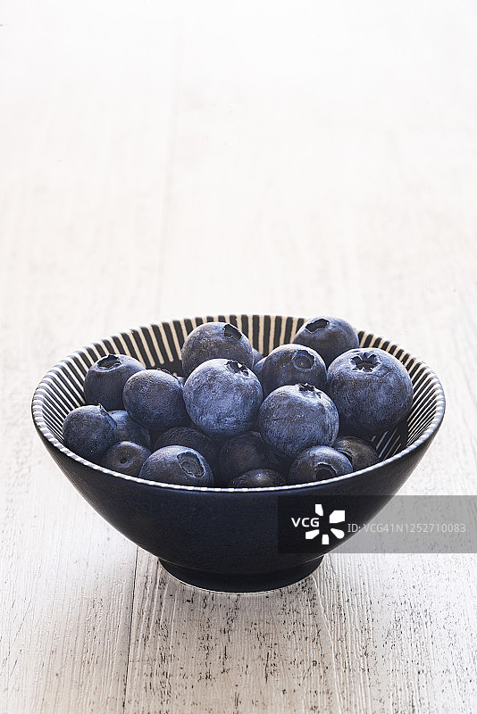 白色木质背景上盛满蓝莓的碗图片素材
