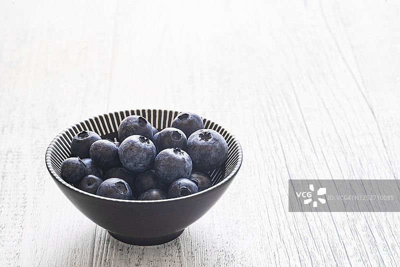 白色木质背景上盛满蓝莓的碗图片素材