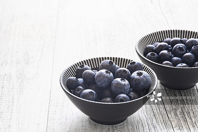 白色木质背景上的几碗蓝莓，背光拍摄图片素材