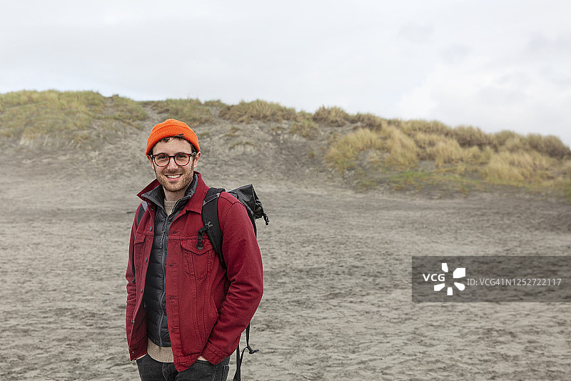 穿红色牛仔夹克、背背包的年轻男人海滩肖像图片素材