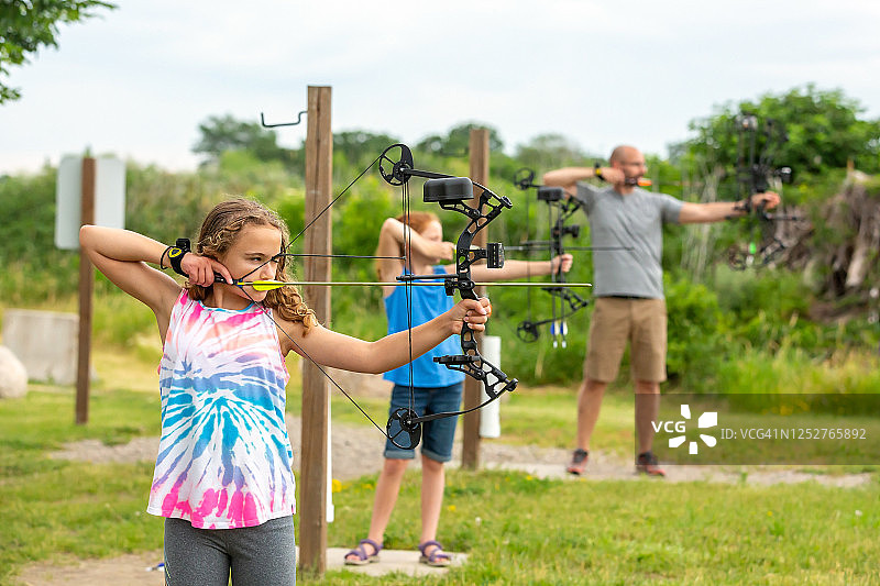 两个女孩和爸爸在户外射箭场练习图片素材