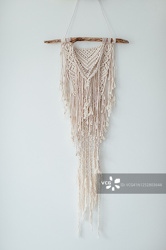 一个米色100％纯棉手工macrame panno装饰挂在白色的墙壁上。设计家居装饰。波西米亚概念。图片素材