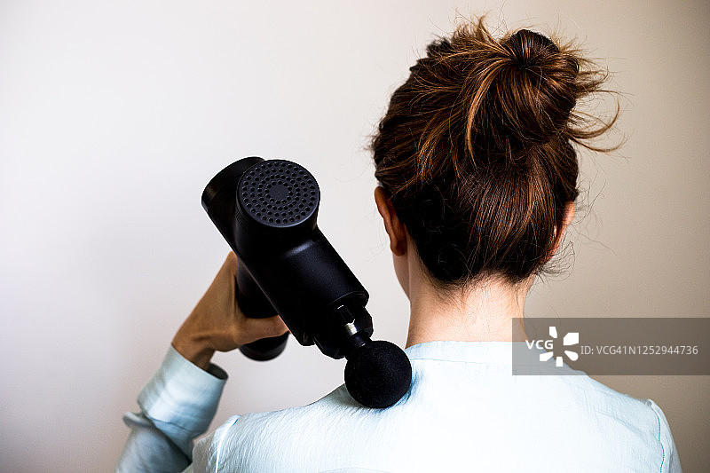 使用按摩枪/按摩器的女子的背影图片素材