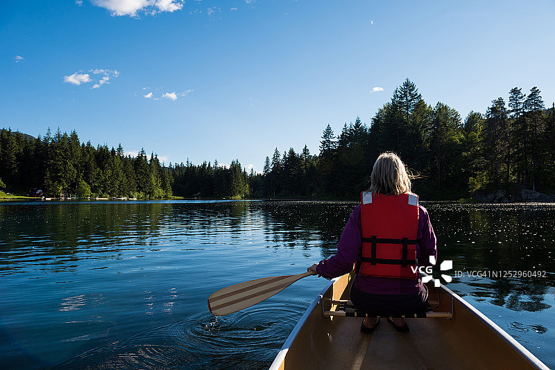 女人在山间湖泊上划独木舟图片素材