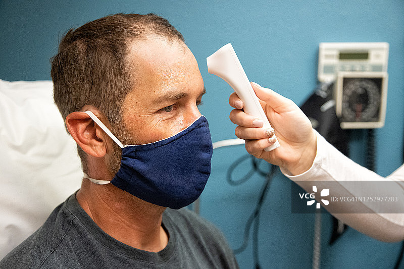 女护士在诊室用红外额温计为戴口罩的白人男子测温图片素材