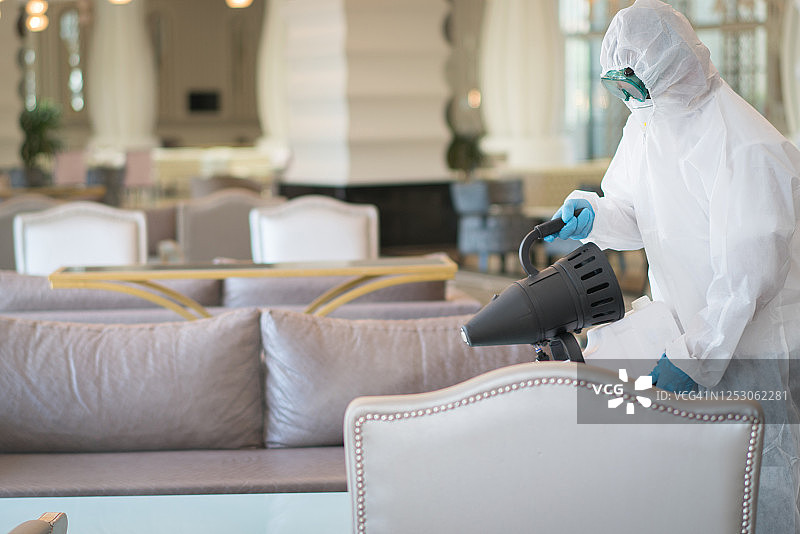 身穿防护服的男人在酒店消毒家具图片素材