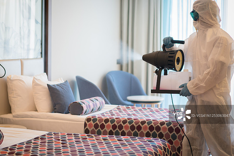 身穿防护服的男子在酒店房间内消毒图片素材