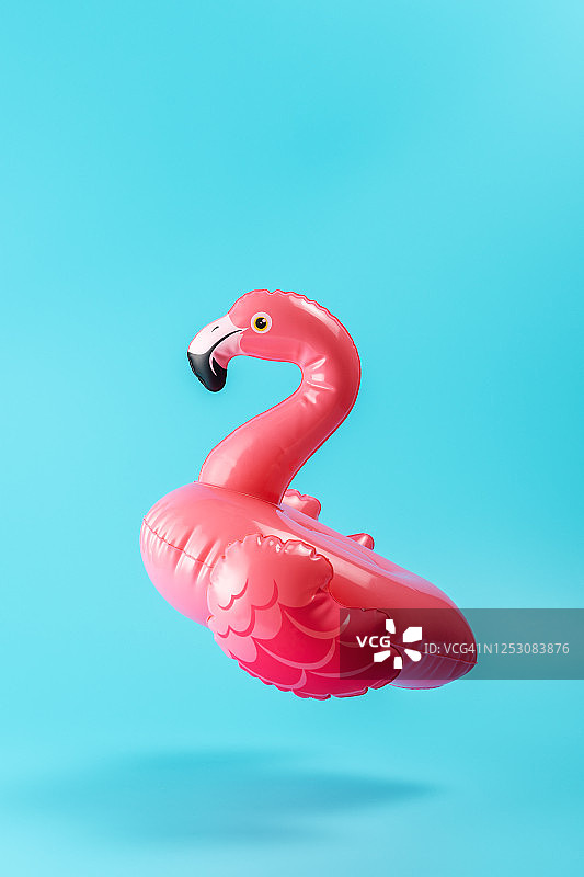 蓝色背景上的充气火烈鸟泳池玩具：简约夏季概念图片素材