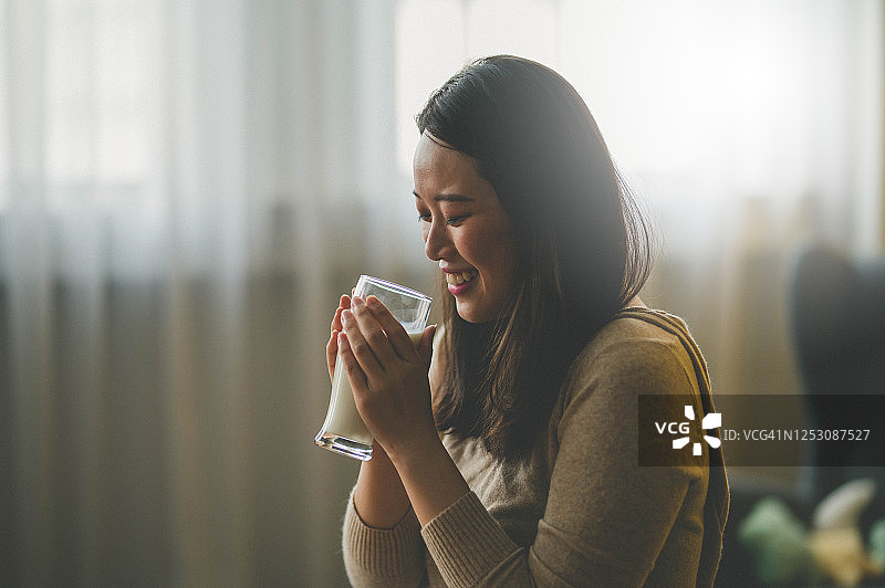 快乐的年轻亚洲女性在客厅享用牛奶图片素材