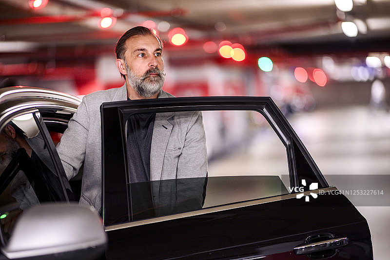 一位公司 CEO 走出他在停车场里的豪华轿车图片素材