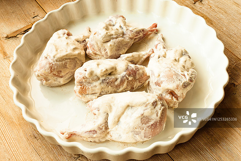 白色盘子上，木质背景上，预备烹饪的生鹌鹑，配以酸奶油图片素材