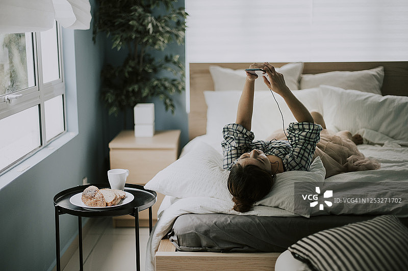 中国女人在早上躺在床上用智能手机听音乐图片素材