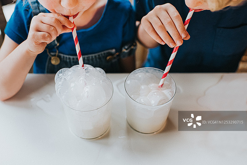 孩子们用纸吸管往一杯牛奶里吹泡泡图片素材
