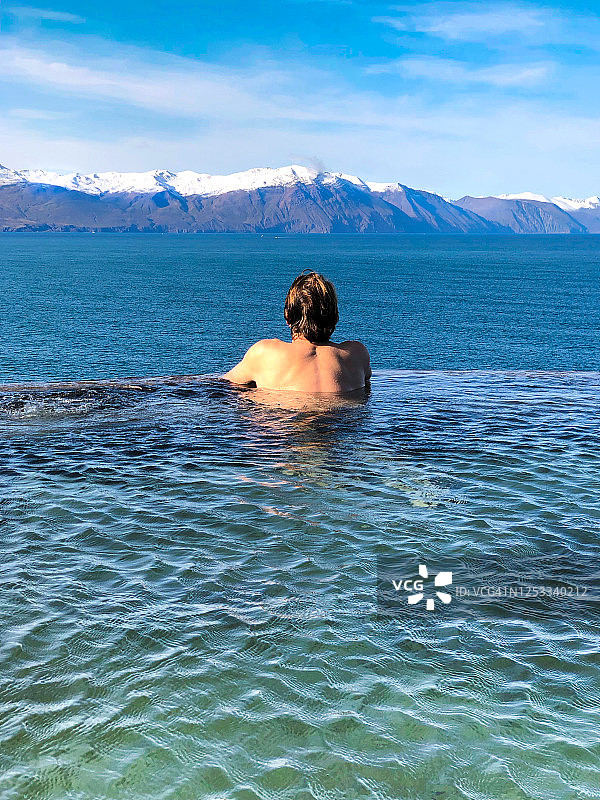 男子浸泡在冰岛温泉中，远处是雪山图片素材