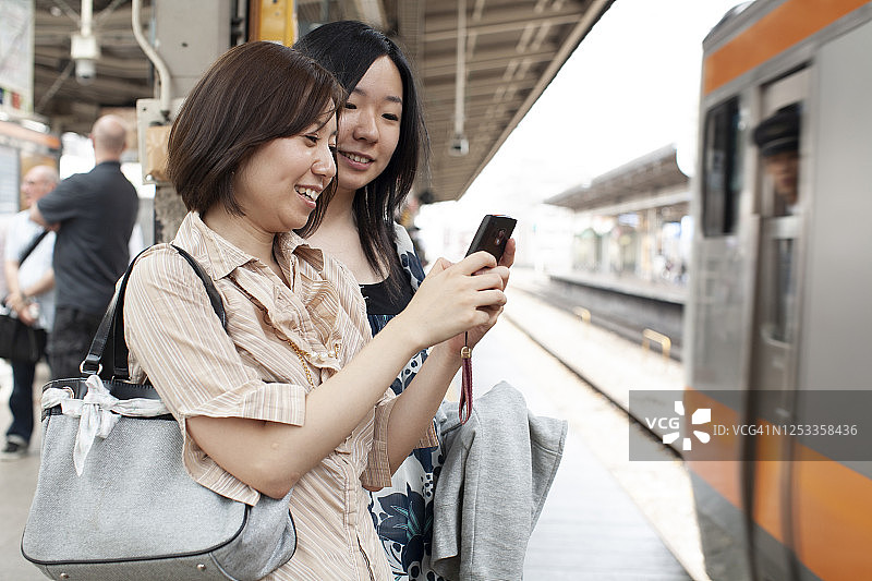 两个二十多岁的女孩在地铁旁使用手机图片素材