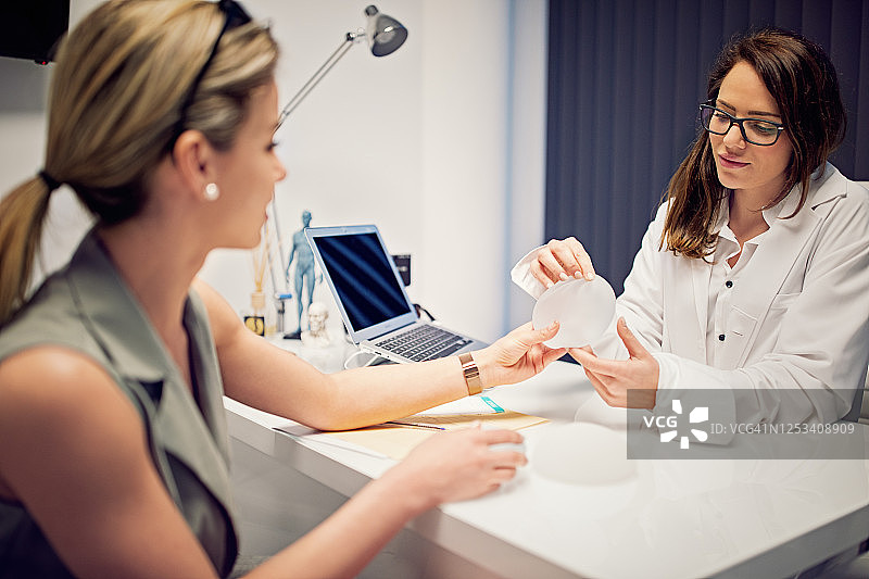 医生在美容诊所向年轻女人展示隆胸假体图片素材