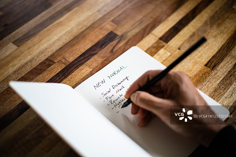 在笔记本上书写“新常态”清单的手部特写图片素材
