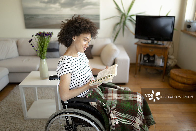 快乐的非裔美国妇女坐在轮椅上读书图片素材