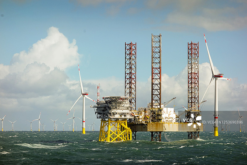 北海大型海上8兆瓦风力涡轮机壮丽景色，海浪中带有自升式船舶和海上平台的水平线上的风力发电场图片素材