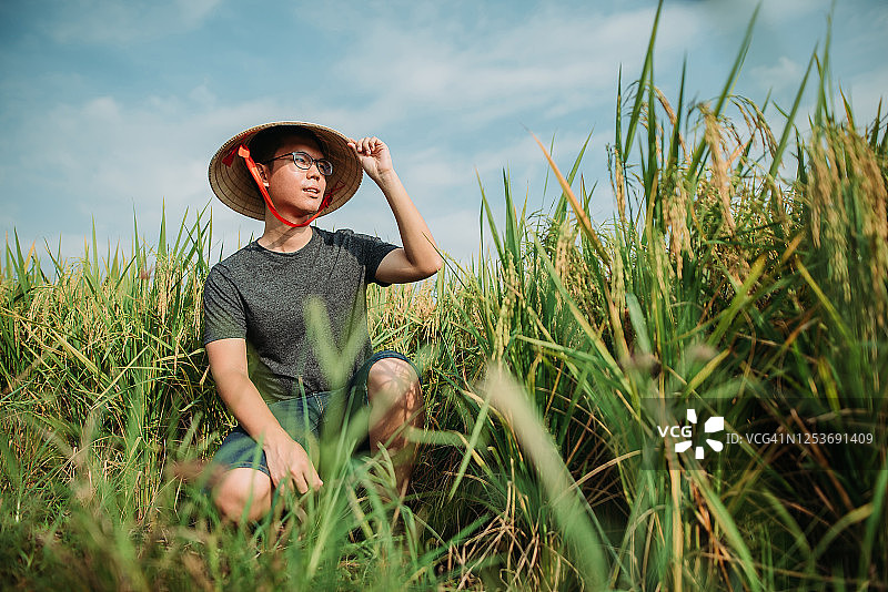手持藤帽跪在稻田里的亚洲农民图片素材