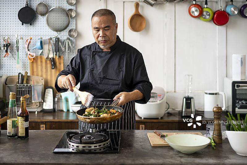 一个亚洲中年厨师在厨房烹饪图片素材